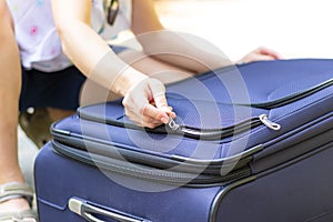 Women`s hands open a suitcase with things on a forest road on a summer sunny day. Close-up