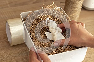 Women`s hands pack an angel figure in a white box with craft paper