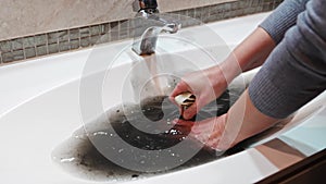 women's hands with plunger and dirty sink with the clog in the pipe.