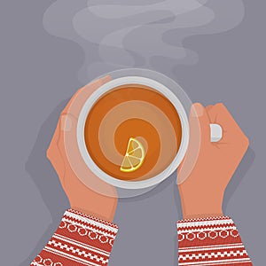 Women`s hands in a red sweater are warming, gently holding a cup of black tea with a slice of lemon. View from above.