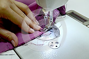 Women`s hands sew on a white sewing machine from pink-black fabric.