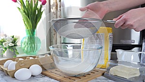 Women's hands sift wheat flour through a sieve