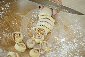 Women`s hands slice with knife cinnamon dough roll for homemade baking