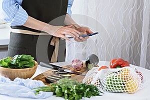 Women`s hands with smartphone in kitchen, cooking vegetables, cooking at home