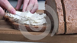 Women's hands smear bread with cream cheese on a wooden board.