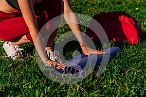 Women`s hands spread out a sports mat on green grass in the park concept of outdoor workouts