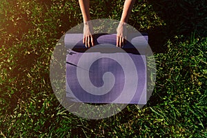 Women`s hands spread out a sports mat on green grass in the park concept of outdoor workouts