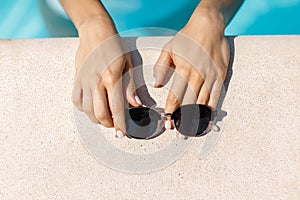 Women`s hands and sunglasses in the swimming pool