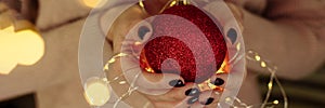 Women& x27;s hands in a sweater hold a Christmas ball with garland lights. New year and christmas concept. Copy space