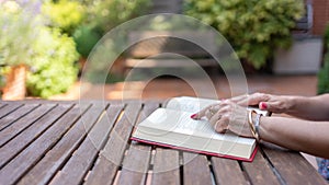 Women& x27;s hands on top of a book on a garden wooden table on a summer day.