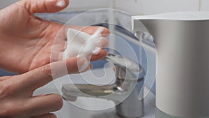 Women`s hands use an automatic dispenser with liquid soap and wash under water.