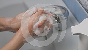 Women`s hands use an automatic dispenser with liquid soap and wash under water.