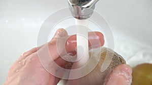 Women`s hands wash kiwi fruit in the sink or washbasin close-up.