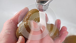 Women`s hands wash kiwi fruit in the sink or washbasin close-up.