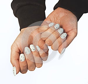 Women`s hands with white gel polish and black fragments on nails.