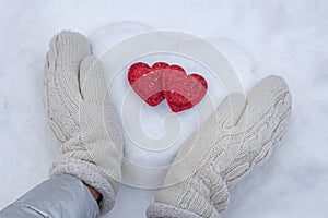 Women`s hands in white knitted mittens with a red heart made of snow on a winter day. Love concept. Valentine day background