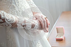 Women`s hands on a white wedding dress. show her wedding ring with box in background.