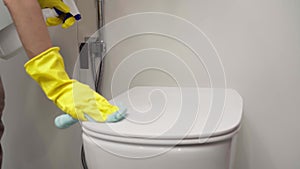 Women's hands in yellow gloves wipe the toilet bowl in the bathroom with a rag.