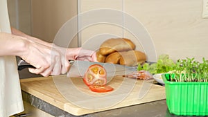 Women`s hanWomen`s hands cut tomatoes for making sandwiches on a wooden cutting board.