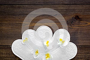 Women`s hygiene products. Critical days concept. Sanitary pads near small flowers on dark wooden background top view