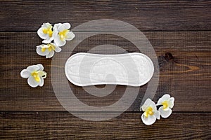 Women`s hygiene products. Critical days concept. Sanitary pads near small flowers on dark wooden background top view