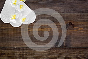 Women`s hygiene products. Critical days concept. Sanitary pads near small flowers on dark wooden background top view