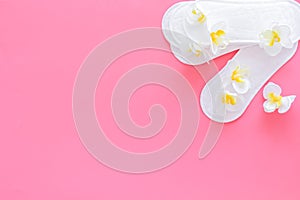 Women`s hygiene products. Critical days concept. Sanitary pads near small flowers on pink background top view copy space