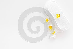 Women`s hygiene products. Critical days concept. Sanitary pads near small flowers on white background top view copy