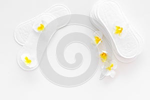 Women`s hygiene products. Critical days concept. Sanitary pads near small flowers on white background top view copy