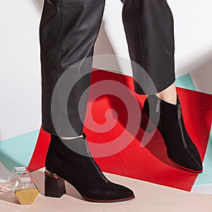 Women& x27;s legs in black pants and black short shoes on medium heel stands in the studio against a colored background