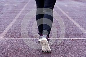 Women`s legs in black sports leggings and sports shoes on a treadmill of a sports open stadium