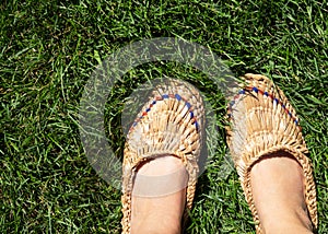 Women`s legs are dressed in a pair of old bast shoes stand on the grass.
