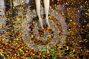 Women`s legs in fishnet tights in gold shoes on a gold floor from confetti