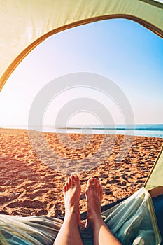 Women`s legs out of the tent. Vacation camping on the sea sandy beach