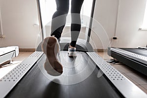 Women`s legs run on a treadmill. Young woman engaged in fitness in the gym. Girl in training in the gym. Back view.