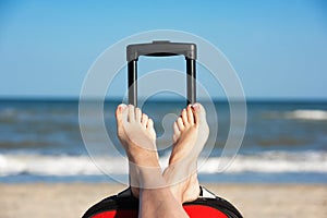 Women`s legs in shoes on a travel suitcase in the ocean background.