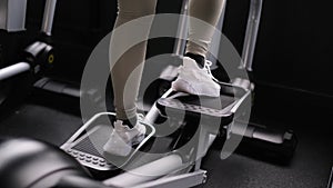 Women's legs in sneakers work on a stepper in the gym. The concept of sport and healthy lifestyle. The girl is doing