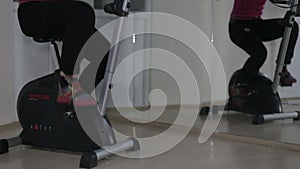 Women's legs in sport shoes pedaling on a stationary bike in the gym