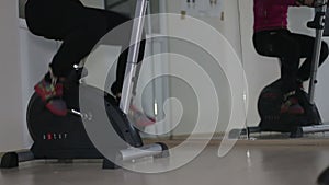 Women's legs in sport shoes pedaling on a stationary bike in the gym