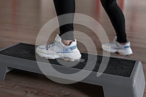 Women`s legs in stylish sporty white sneakers stand on the platform steps in the gym. Young woman trains in a fitness studio.