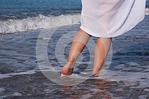 Women& x27;s legs walk along the beach in summer. Close-up of barefoot young adult woman in a pareo.