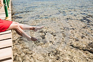 Women`s legs at wooden pier over sea water on summer resort. Summer vocation.