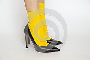 Women's legs in yellow socks and black high -heeled shoes on a white background, fashionable shoes