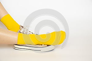 Women's legs in yellow socks and summer sports sneakers on a white background, fashion