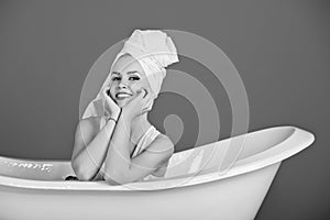 Women`s leisure. happy woman with towel turban sitting in white bathtub