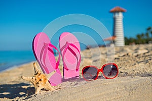 Women's marine accessories: sandals, sunglasses and starfish on tropical sand beach against the background of lighthouse