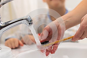 Women`s mother`s hands help the child brush his teeth before going to bed at home in the bathroom in the sink