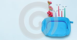 Women`s multi-colored disposable razors, cosmetic bag, pink flowers on a pastel blue background, top view Flat lay copy space.