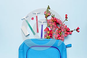 Women`s multi-colored disposable razors, cosmetic bag, pink flowers on a pastel blue background, top view Flat lay copy space.