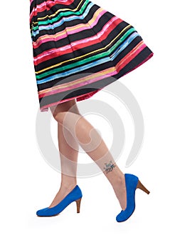 Donna multicolore vestito e gambe in blu tacchi alti e drum kit tatuaggio sulla gamba.